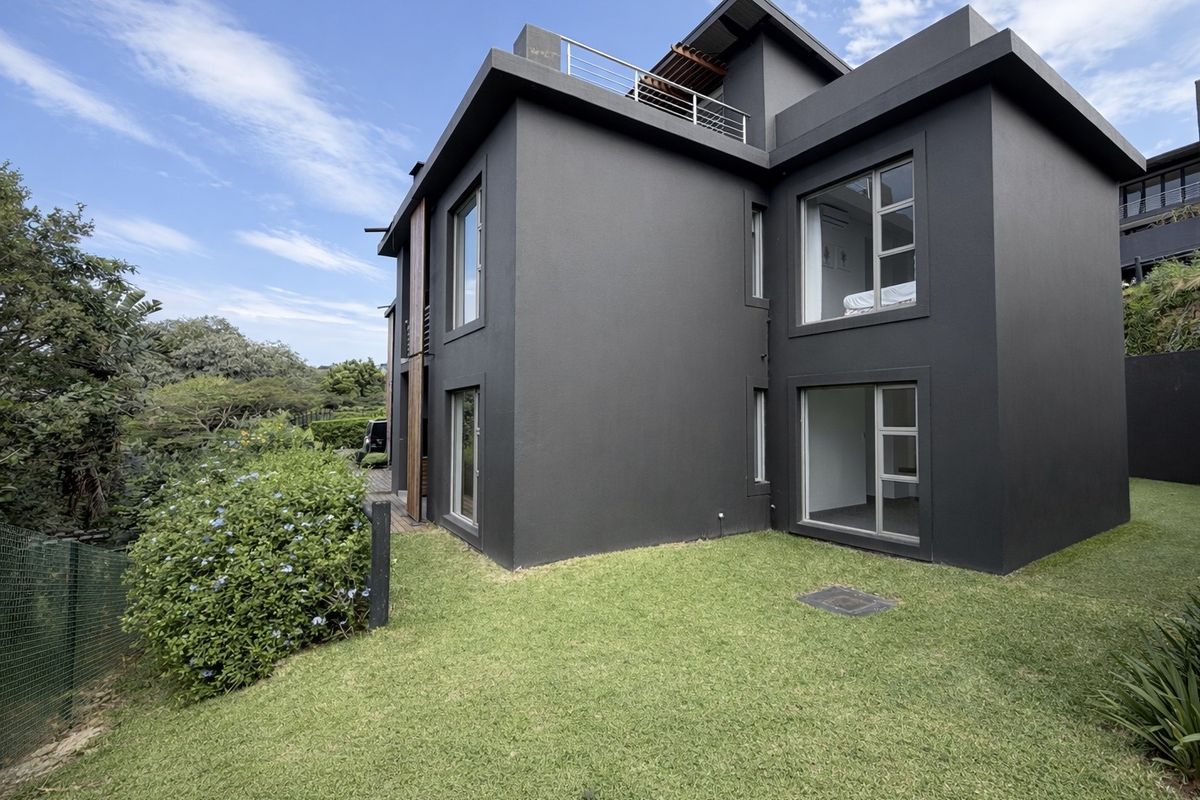 A modern two-story apartment exterior featuring a dark facade, large windows, and a private rear lawn area.