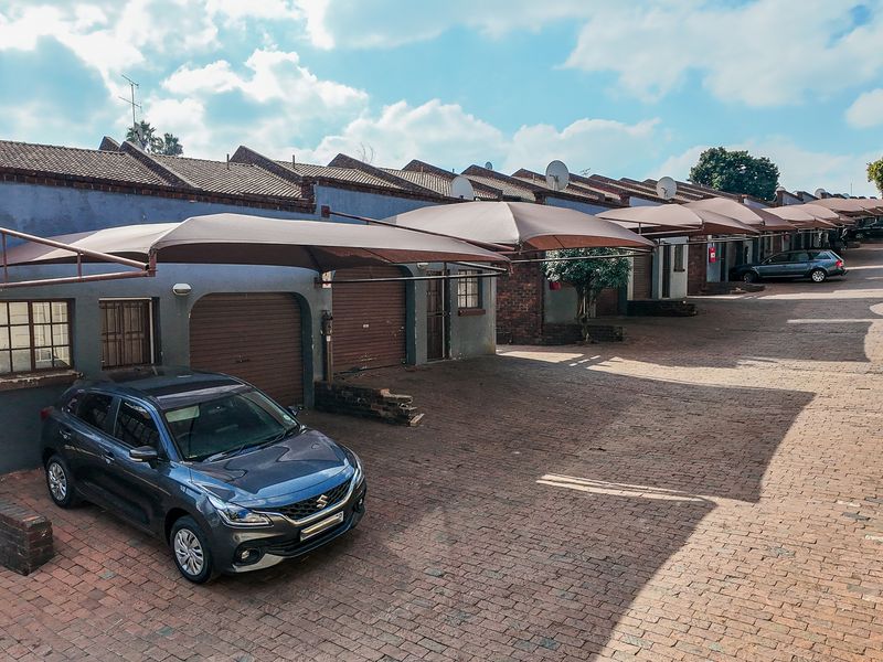 Exterior view of a townhouse complex featuring a brick-paved driveway, multiple roller shutter garage doors, and installed shade cloth carports.