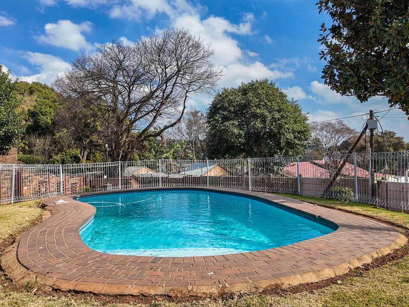 A private swimming pool area featuring a curved brick surround and secure metal perimeter fencing with integrated razor wire.