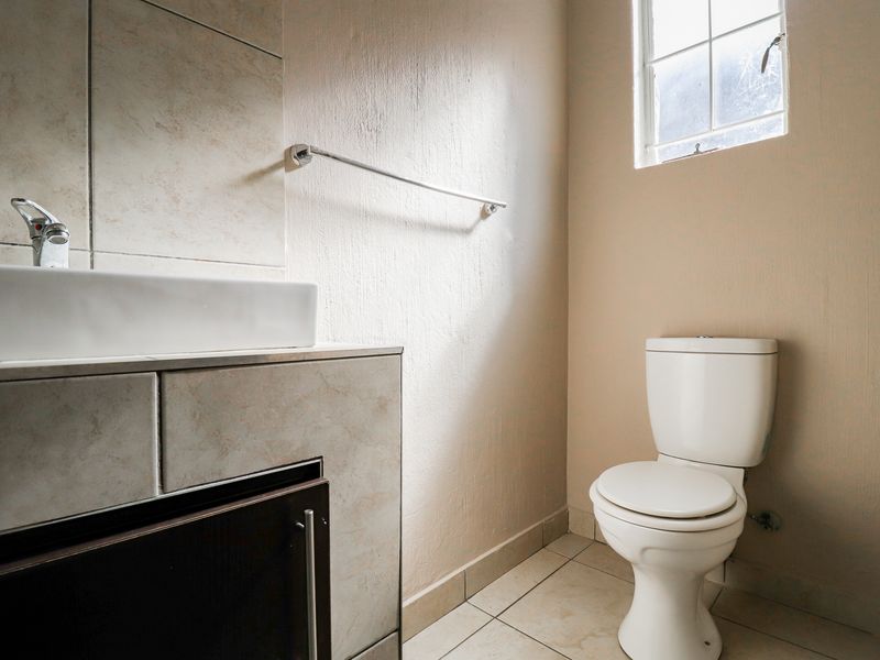 A functional bathroom featuring a vanity with a basin, tiled splashback, and a standard toilet, finished with neutral floor tiles.