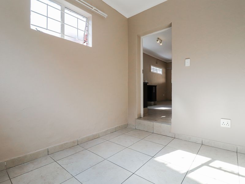 A clean, empty utility space featuring neutral wall paint, tiled flooring, and a window with security bars, providing a versatile area for various uses.