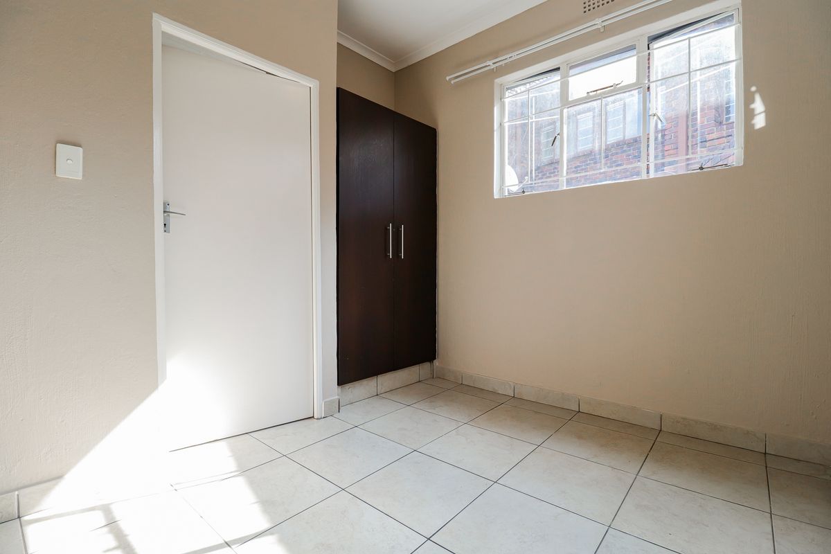 A bright, empty bedroom featuring neutral wall paint, tiled flooring, and a built-in dark wood cupboard.