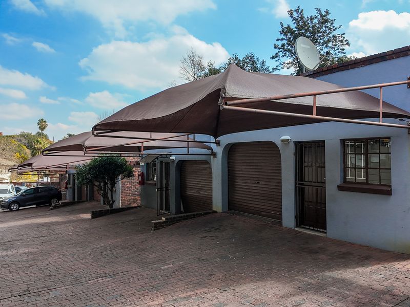 Exterior view of a townhouse garage area featuring roller shutter doors, a shade sail carport structure, and brick paved driveway.