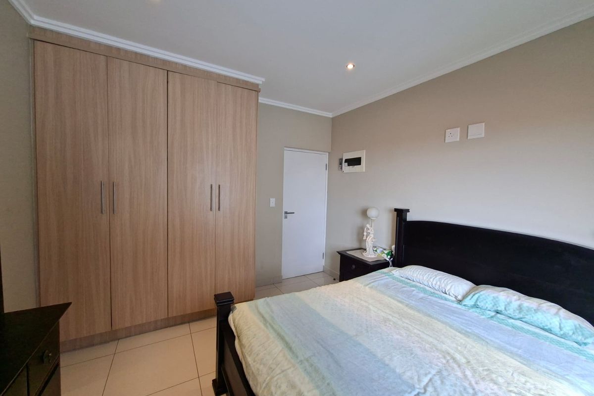 A well-maintained bedroom featuring light wood-finish built-in cupboards, neutral tiled flooring, and recessed ceiling lighting.