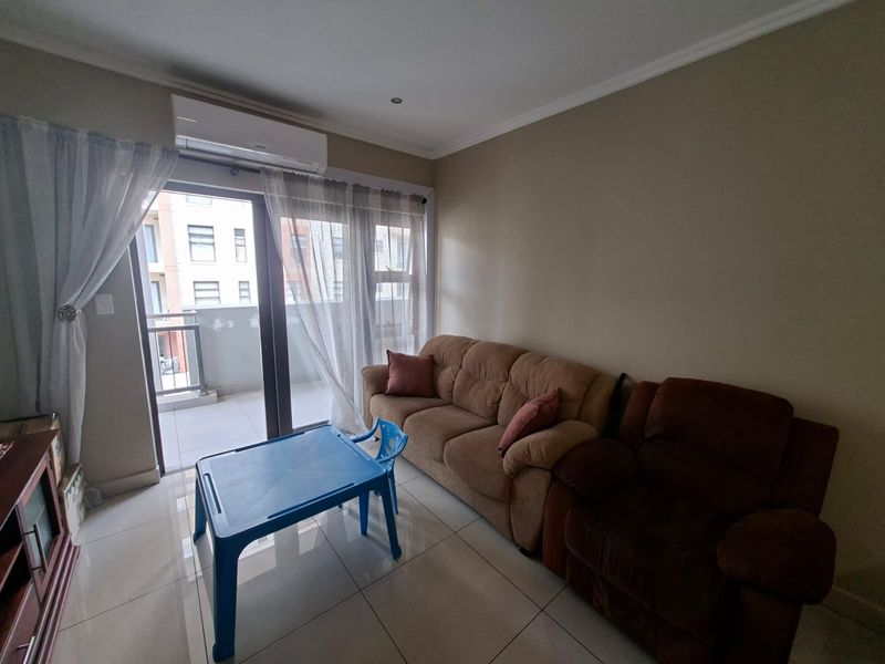 A living room featuring tiled flooring, a wall-mounted air conditioning unit, and a sliding glass door providing access to an outdoor balcony.