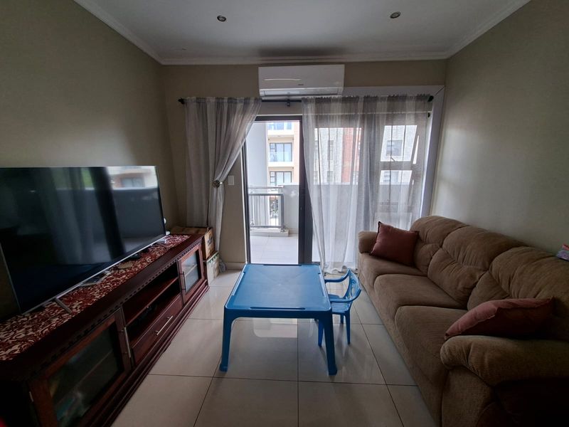 A well-lit living room featuring tiled flooring, a split-system air conditioner, and direct access to an outdoor balcony through a sliding glass door.