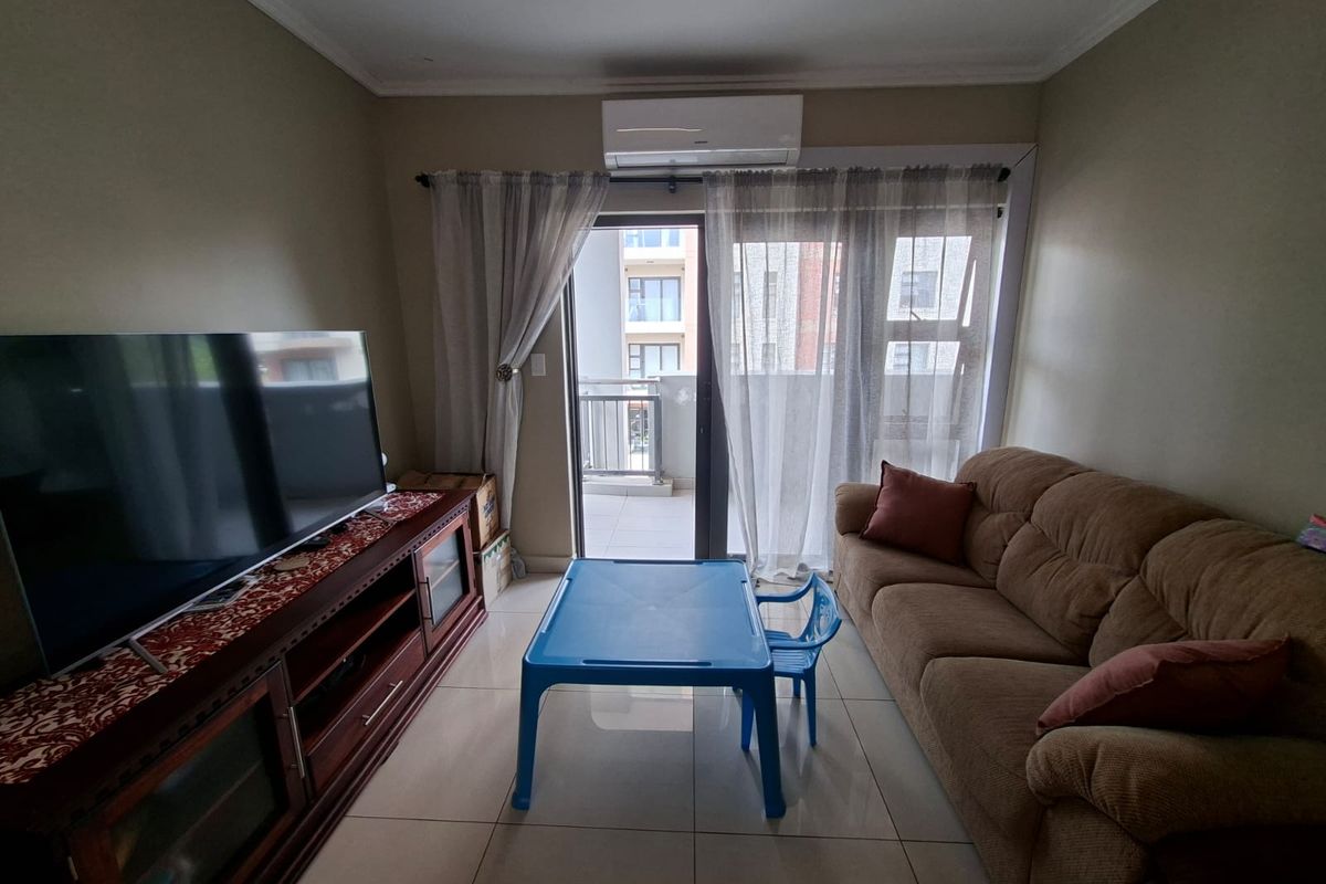 A well-lit living room featuring tiled flooring, a split-system air conditioner, and direct access to an outdoor balcony through a sliding glass door.