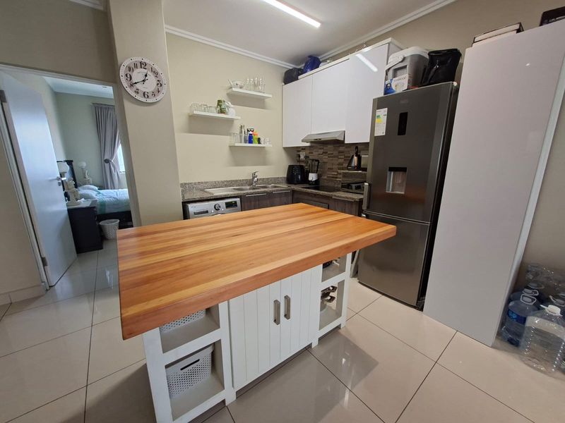 Modern kitchen featuring granite countertops, built-in cabinetry, a central wooden-topped island, and tiled flooring, providing a functional and well-maintained cooking space.