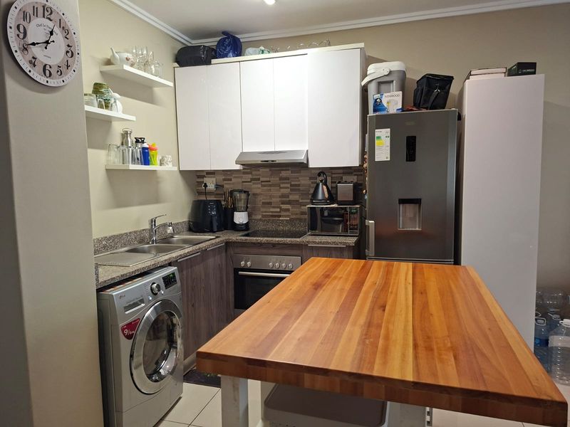 Compact kitchen featuring modern white and wood-grain cabinetry, stone countertops, integrated appliances, and a functional layout with a central wooden island.