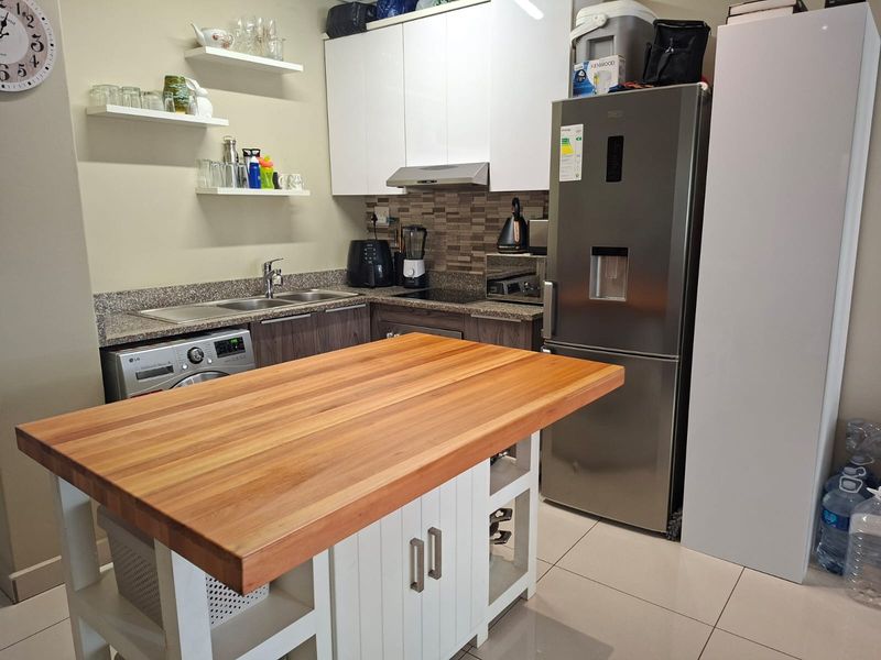 Compact kitchen featuring granite countertops, tiled backsplash, white upper cabinetry, and a central wooden island, providing functional workspace and storage.