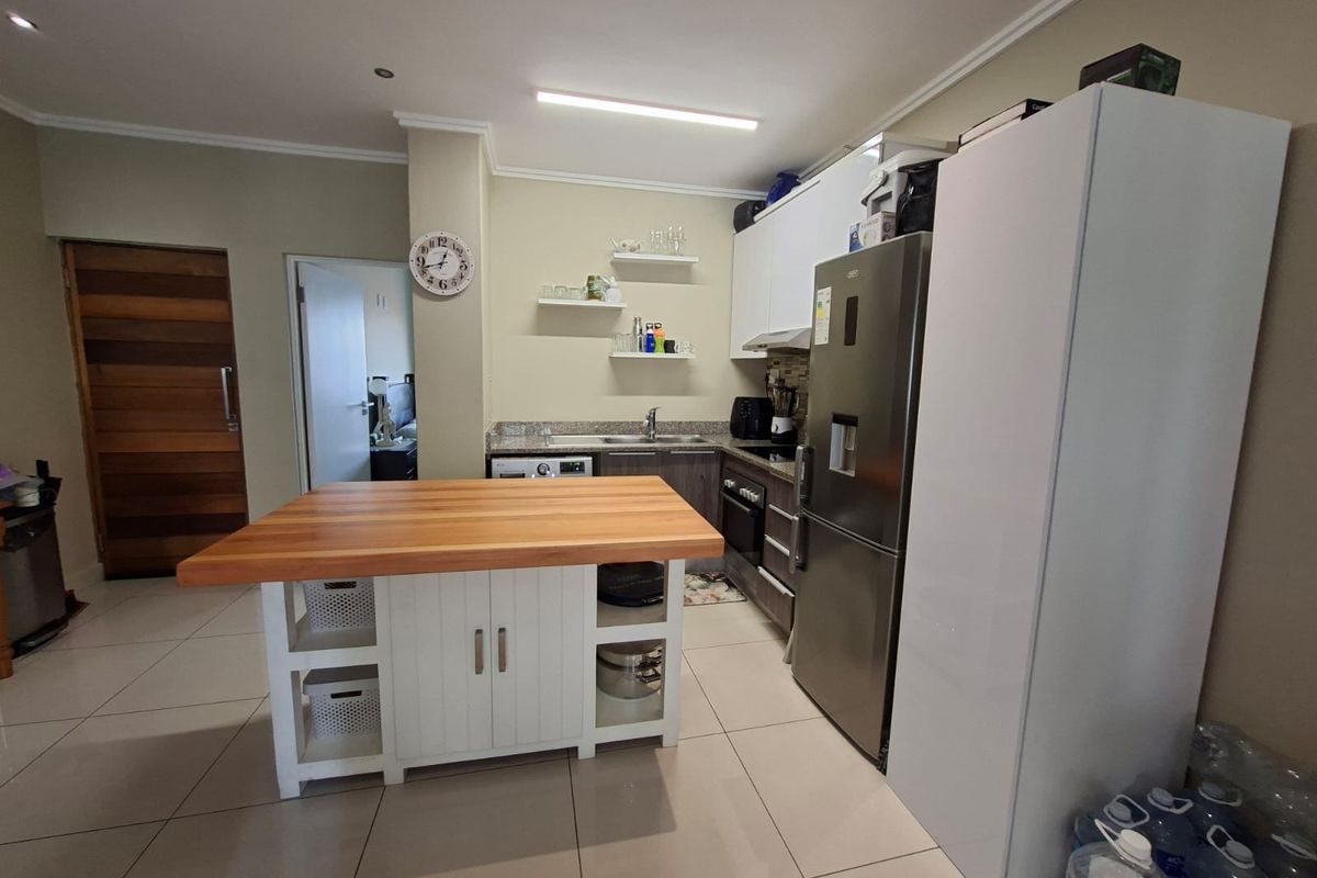 A functional kitchen featuring built-in cabinetry, stone countertops, a central island with a wooden top, and integrated appliances, finished with neutral tiled flooring.
