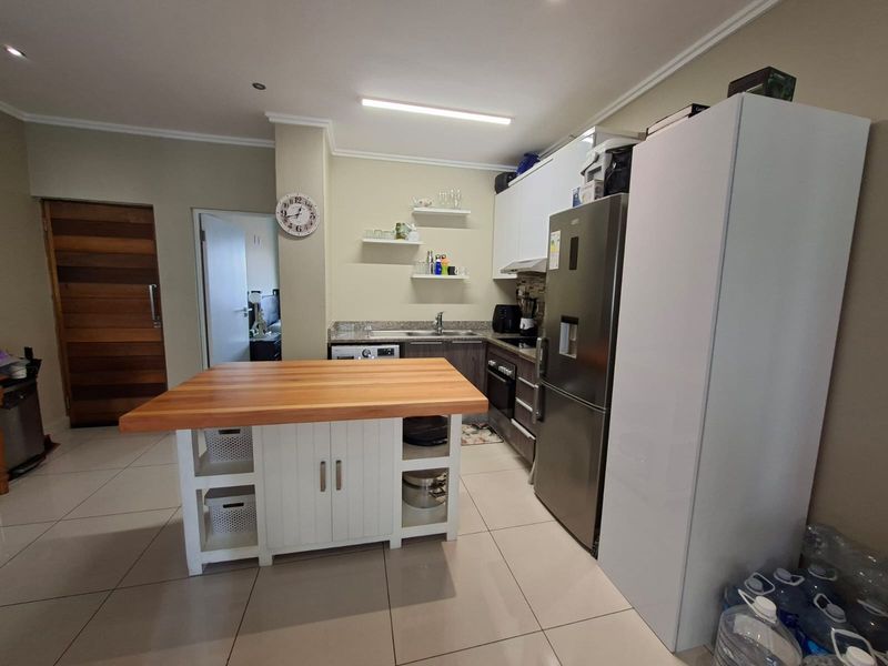 A functional kitchen featuring built-in cabinetry, stone countertops, a central island with a wooden top, and integrated appliances, finished with neutral tiled flooring.
