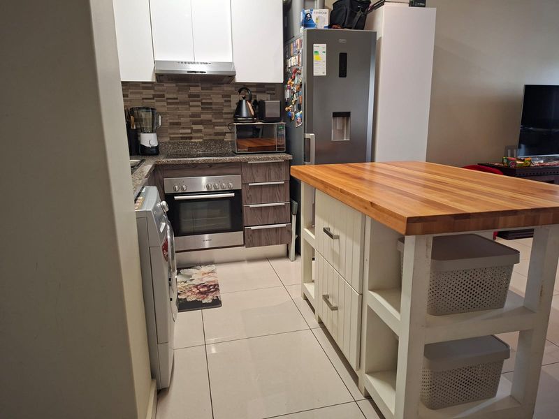 A functional kitchen featuring modern cabinetry, stone countertops, a tiled backsplash, built-in oven, extractor fan, and a central kitchen island with wooden top.