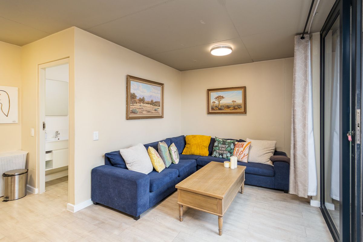 A well-maintained living room featuring light laminate flooring, a neutral color palette, and direct access to an adjacent bathroom and outdoor area.