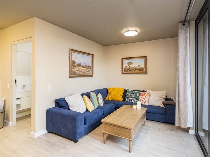 A well-maintained living room featuring light laminate flooring, a neutral color palette, and direct access to an adjacent bathroom and outdoor area.