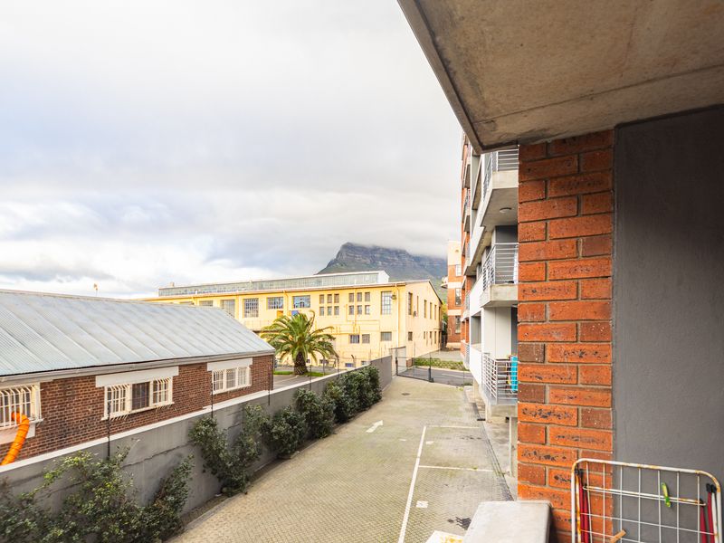A view from a balcony overlooking a paved driveway and neighbouring industrial-style buildings with a mountain backdrop.