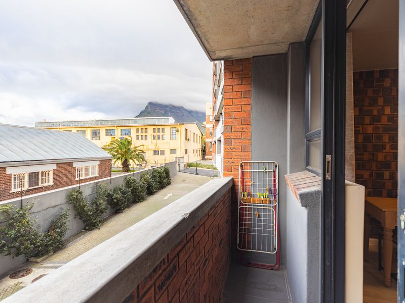 A compact balcony featuring a brick balustrade and concrete ceiling, offering an elevated view of the surrounding urban area and mountain.