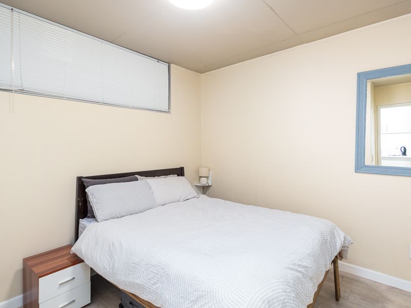 A functional bedroom featuring laminate flooring, neutral wall finishes, and a high-set window with fitted venetian blinds.