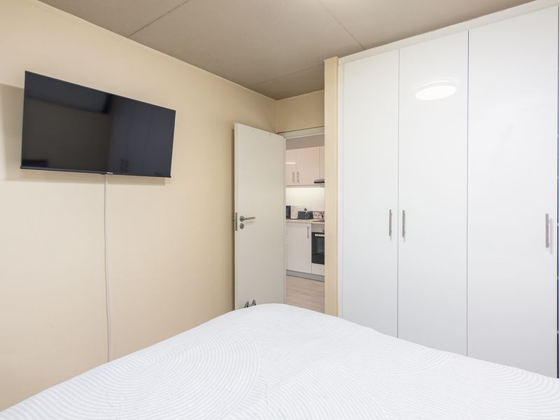 A bedroom featuring a large white built-in wardrobe and a view through the doorway into the adjacent kitchen area.