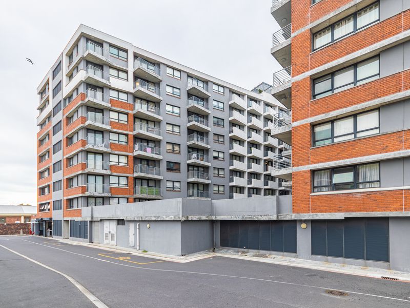 Exterior view of a multi-story apartment complex featuring brick and concrete facade, private balconies, and ground-level parking access.