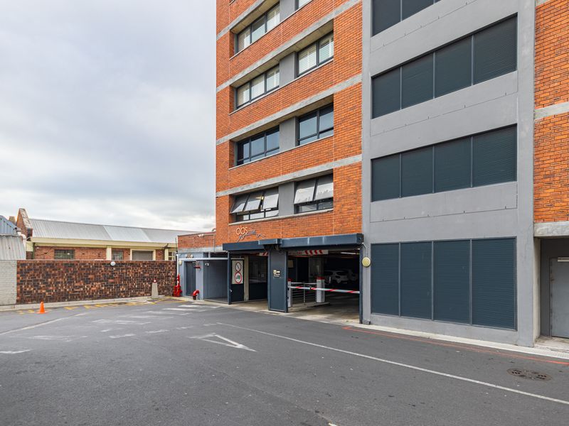 Exterior view of the apartment building entrance, featuring a brick facade, secure parking garage access, and an asphalt driveway.