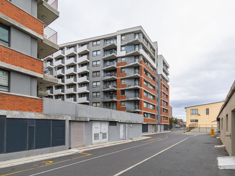 Exterior view of a modern multi-story apartment building featuring brick and concrete facade elements with private balconies and ground-level utility access.