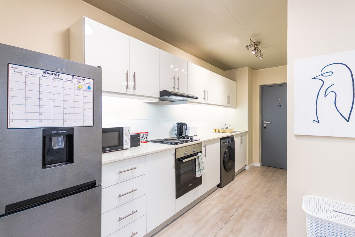 Modern kitchen featuring white cabinetry, stone countertops, built-in oven, gas hob, extractor fan, and integrated washing machine with light laminate flooring.