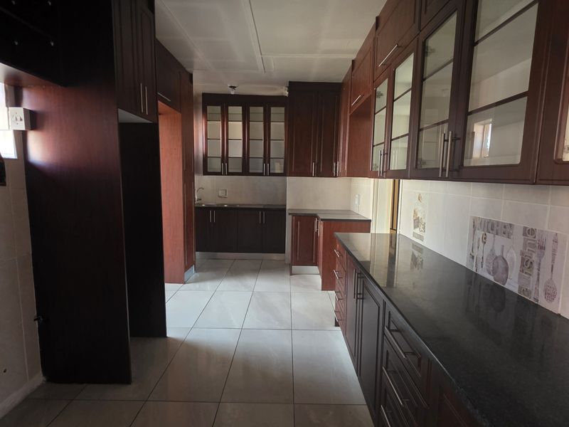 A spacious kitchen featuring dark wood cabinetry, granite countertops, tiled flooring, and a tiled backsplash, offering ample storage and workspace.