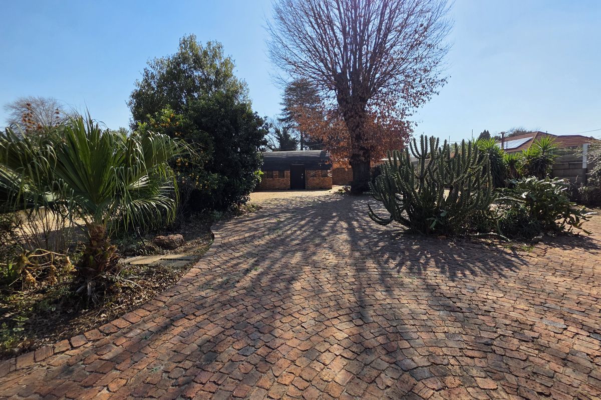 A spacious rear garden area featuring a brick-paved driveway, mature trees, and established landscaping, providing a private outdoor setting.
