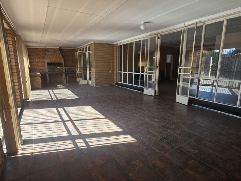 Spacious enclosed patio featuring a built-in brick braai, tiled flooring, and large glass sliding doors providing access to the main living area.