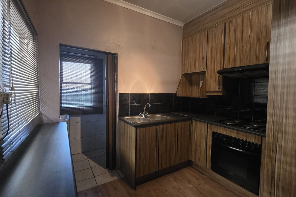 A compact kitchen featuring wood-grain cabinetry, built-in oven and hob, tiled backsplash, and a functional layout with an adjacent utility area.
