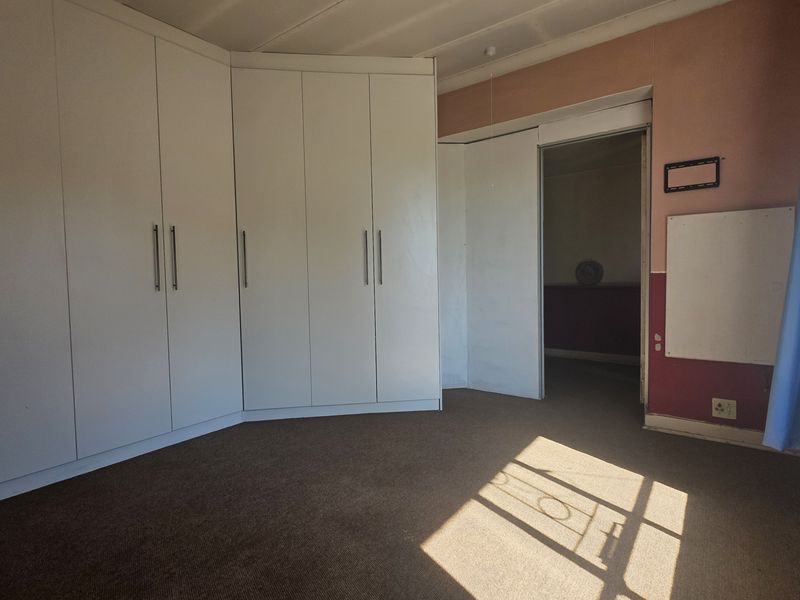 A vacant bedroom featuring extensive built-in cupboard storage, carpeted flooring, and natural light from the side window.
