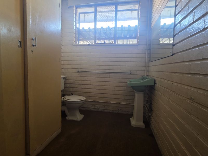 A dated bathroom featuring painted brick walls, a pedestal basin, and a standard toilet, offering potential for modernization and renovation.