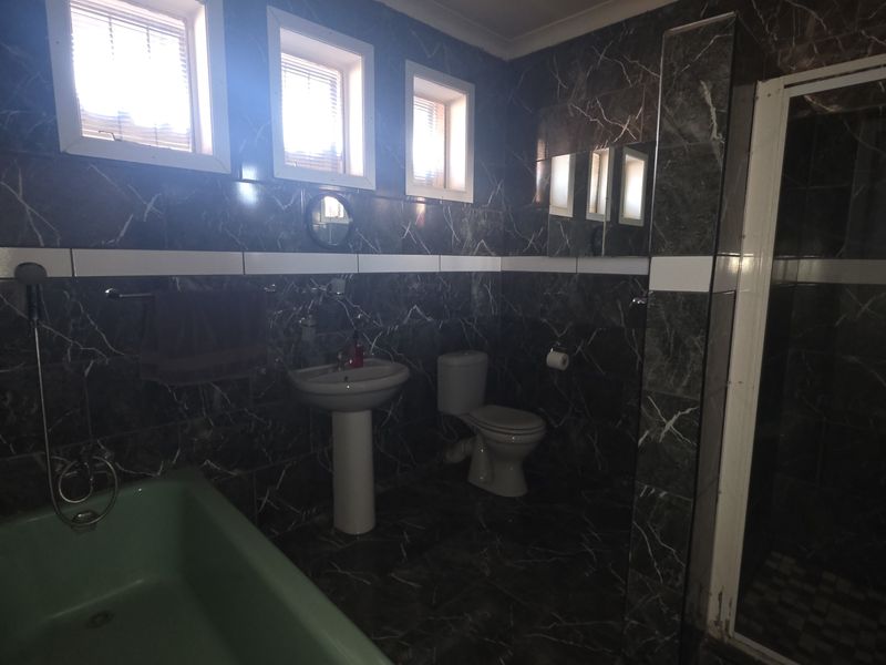 A bathroom featuring dark marble-style wall and floor tiles, a pedestal basin, toilet, bathtub, and a separate shower enclosure with a modern shower panel.