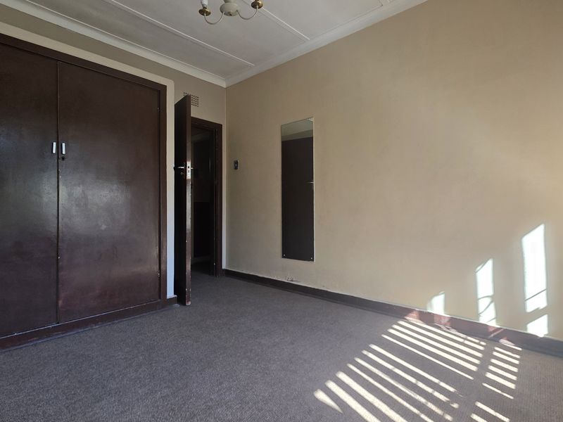 An empty bedroom featuring a built-in wardrobe, carpeted flooring, and coved ceiling details, offering a blank canvas for renovation.