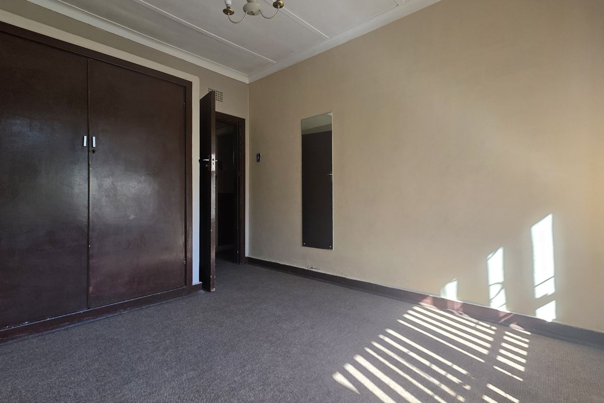 An empty bedroom featuring a built-in wardrobe, carpeted flooring, and coved ceiling details, offering a blank canvas for renovation.