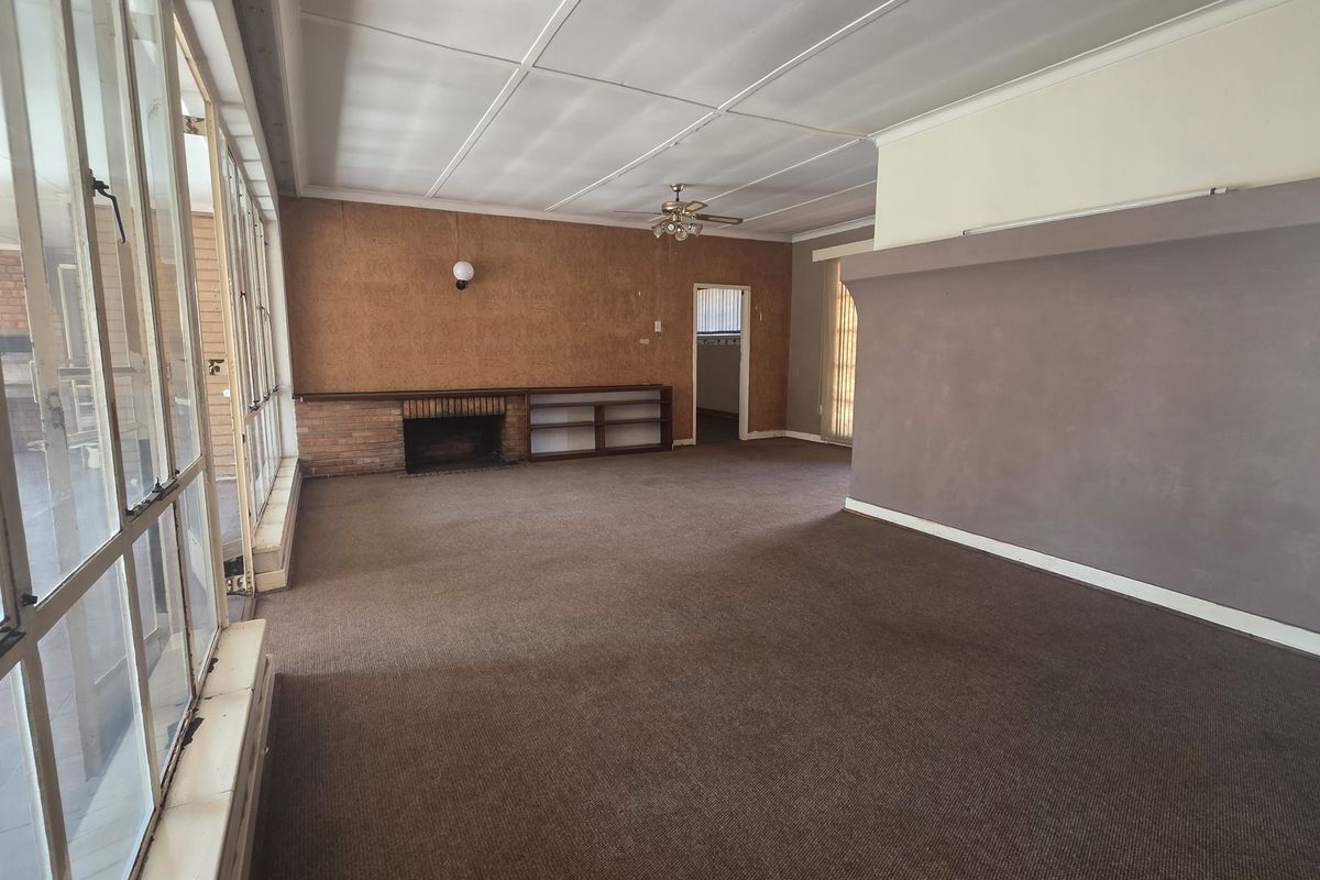 Spacious living area featuring a brick fireplace, built-in shelving, and large glass doors providing natural light. The room is empty and ready for renovation.