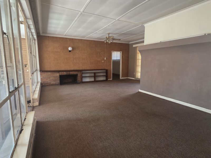 Spacious living area featuring a brick fireplace, built-in shelving, and large glass doors providing natural light. The room is empty and ready for renovation.