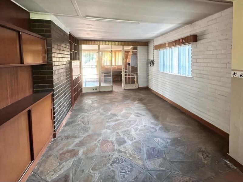 An empty living area featuring rustic flagstone flooring, built-in wooden cabinetry, and a combination of exposed and painted brick walls with glass door access.