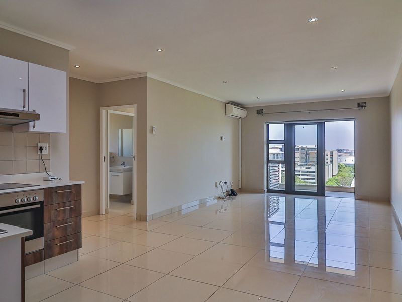 Spacious open-plan living area featuring tiled floors, recessed lighting, and a modern kitchen with built-in appliances, leading to a balcony with city views.