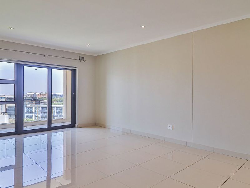 A bright and spacious living area featuring polished tile flooring, recessed lighting, an air conditioning unit, and large sliding doors leading to a balcony.