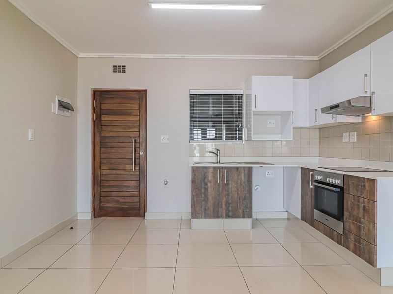 An open-plan kitchen area featuring modern two-tone cabinetry, built-in oven, extractor fan, and tiled flooring, presented in a clean, vacant state.
