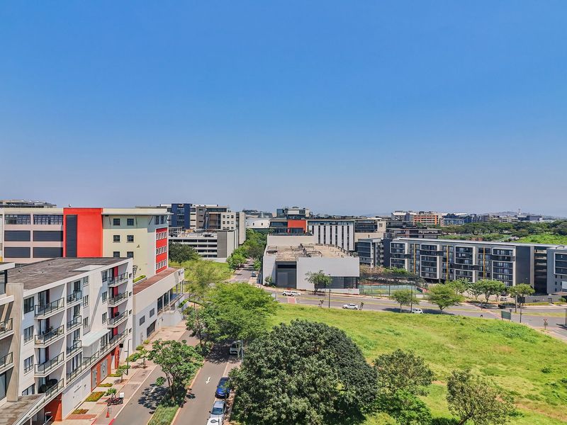 An elevated view overlooking a modern urban apartment complex, surrounding streets, and green landscaped areas.