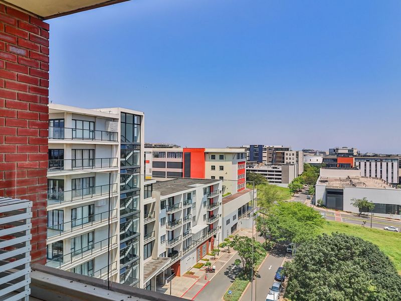 An elevated urban view from a balcony, showcasing surrounding apartment buildings, street infrastructure, and green spaces.