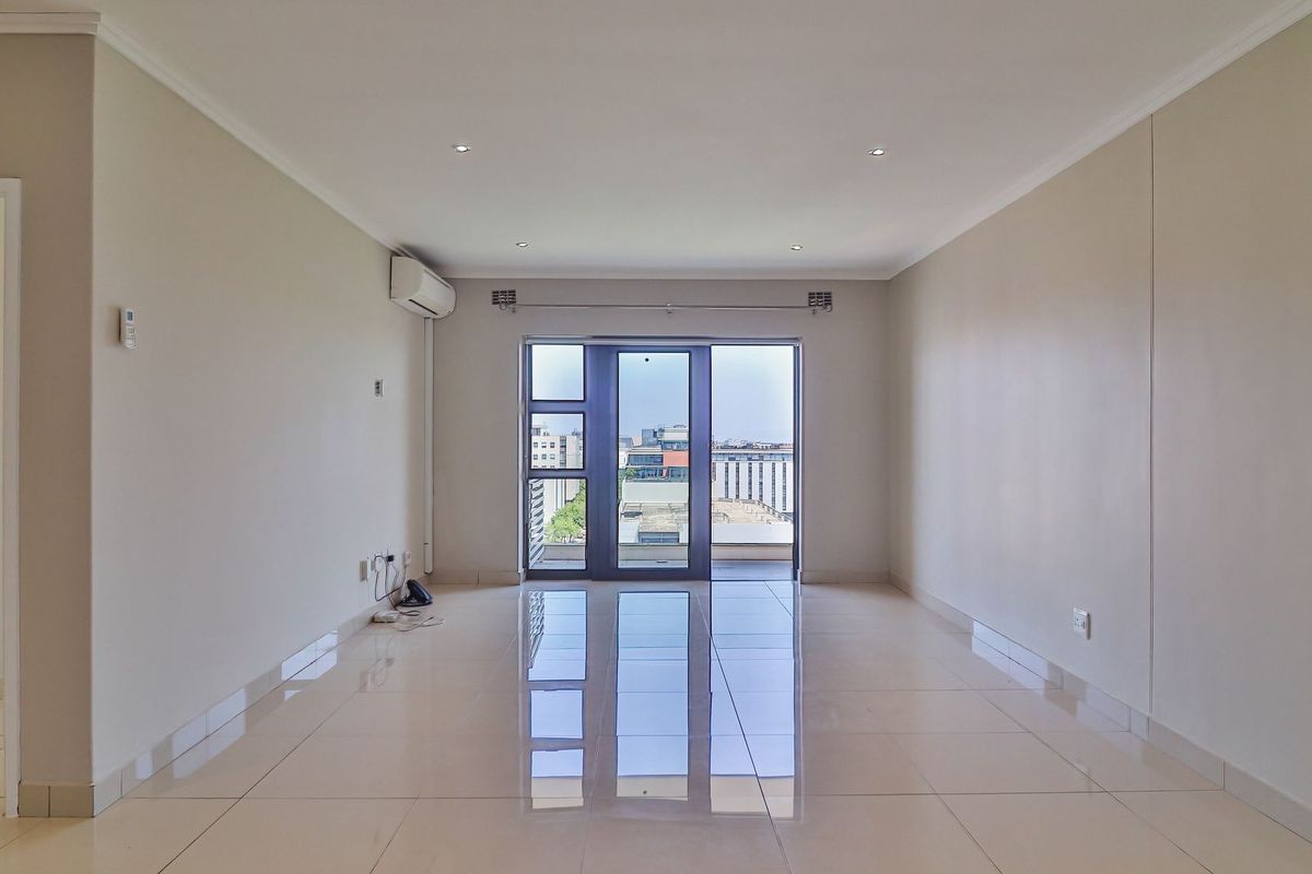 A bright, spacious, and empty living area featuring polished tiled floors, recessed lighting, and a sliding glass door leading to an outdoor balcony.