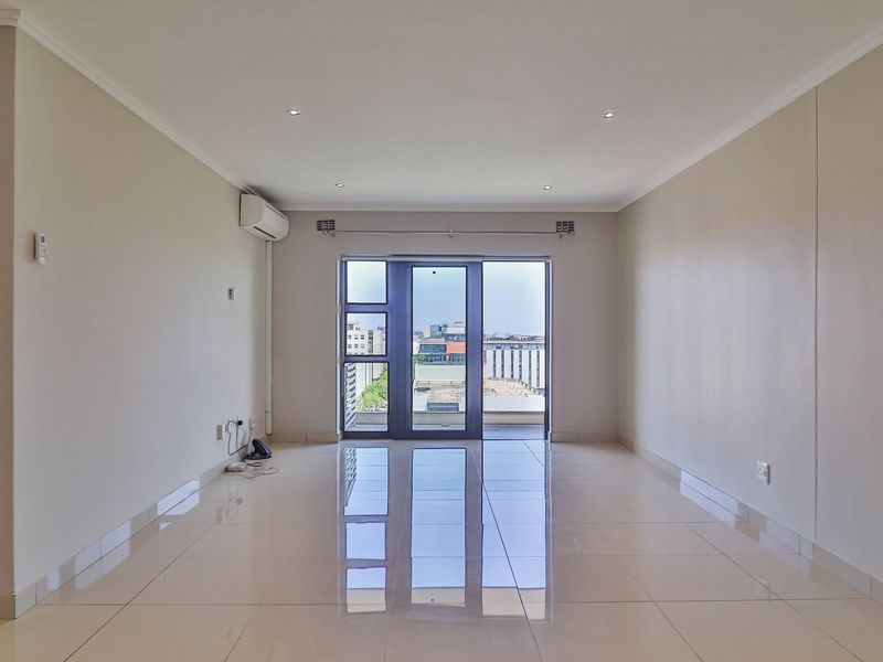A bright, spacious, and empty living area featuring polished tiled floors, recessed lighting, and a sliding glass door leading to an outdoor balcony.