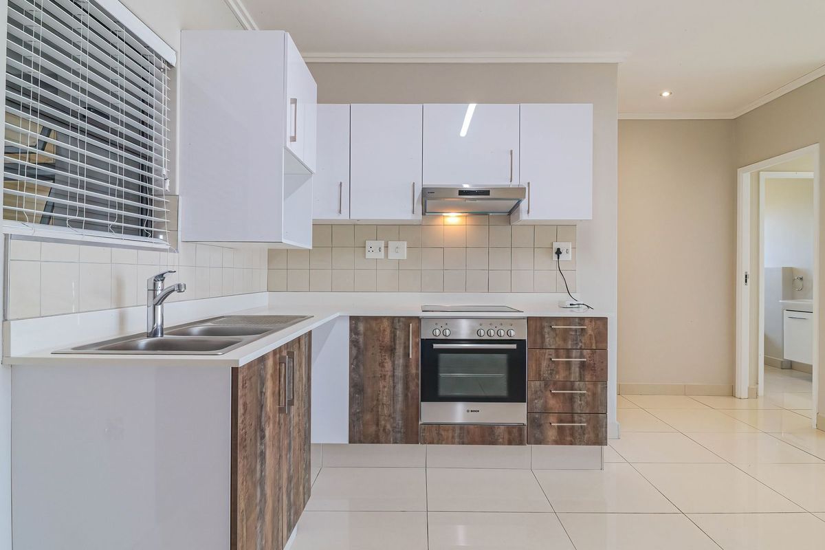 Modern kitchen featuring white upper cabinets, wood-look lower cabinetry, stainless steel appliances, tiled backsplash, and neutral floor tiles.