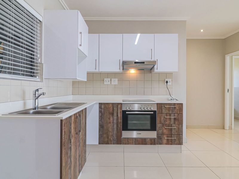 Modern kitchen featuring white upper cabinets, wood-look lower cabinetry, stainless steel appliances, tiled backsplash, and neutral floor tiles.