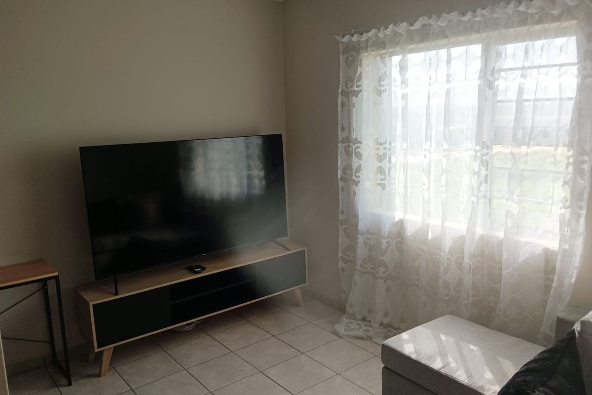 A living room area featuring tiled flooring and a large window allowing natural light into the space.