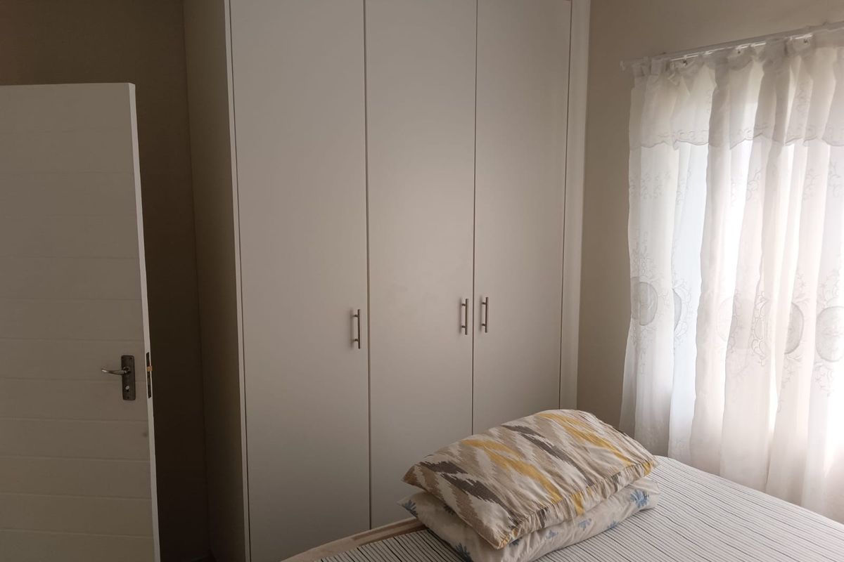A bedroom featuring a clean, white built-in wardrobe with modern handles and natural light from the adjacent window.